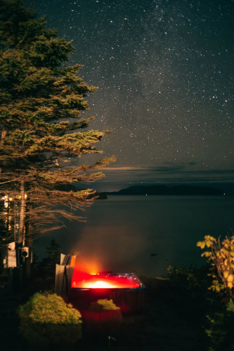 A lit hot tub under a sky full of stars, by the water